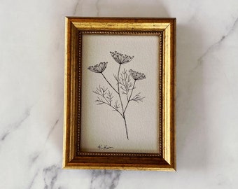 Puede incluir: Un dibujo en blanco y negro de una flor delicada con tres flores. El marco es dorado con un borde decorativo. La firma del artista, "K. Kim", es visible en la esquina inferior derecha.