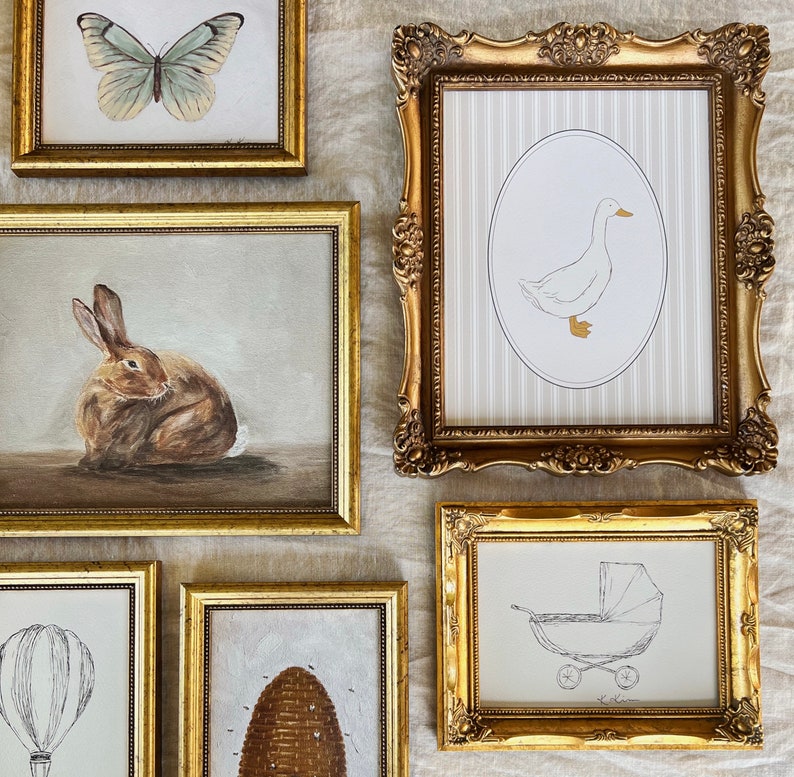 May include: Five gold picture frames with different images inside. The top frame has a white butterfly on a light brown background. The frame to the right has a white duck on a light gray striped background. The frame below the butterfly has a brown rabbit on a light brown background. The frame below the duck has a black and white illustration of a baby carriage on a white background. The frame to the right of the rabbit has a brown beehive on a light brown background.