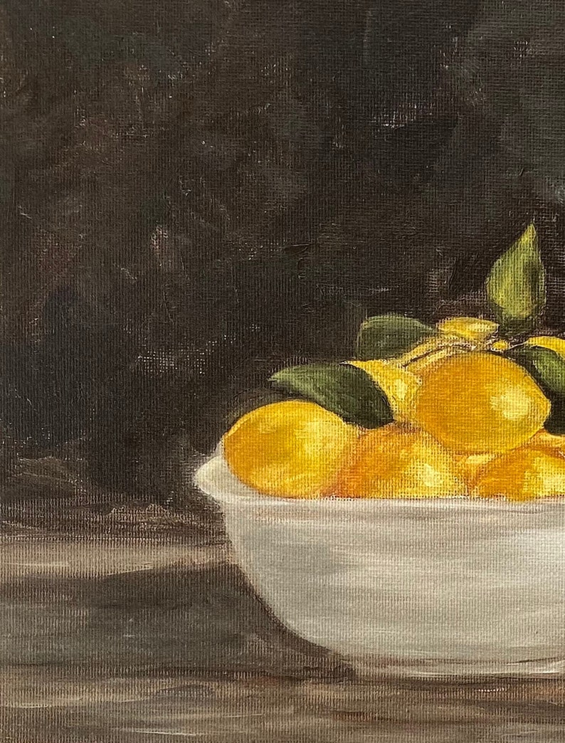 May include: A white ceramic bowl filled with yellow lemons and green leaves. The bowl is sitting on a dark brown wooden surface.