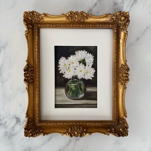 May include: A framed painting of a bouquet of white daisies in a clear glass vase. The daisies are arranged in a simple, elegant way, and the painting is done in a realistic style.
