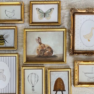 May include: A collection of nine framed illustrations with gold frames. The illustrations include a bee, a butterfly, a rabbit, a duck, a teddy bear, a hot air balloon, a honeycomb, a chicken, and a baby carriage.