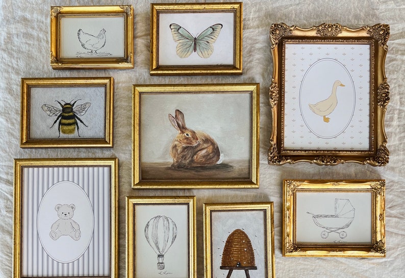 May include: A collection of nine framed illustrations with gold frames. The illustrations include a bee, a butterfly, a rabbit, a duck, a teddy bear, a hot air balloon, a honeycomb, a chicken, and a baby carriage.