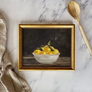 May include: A framed painting of a white bowl filled with yellow lemons on a dark background.