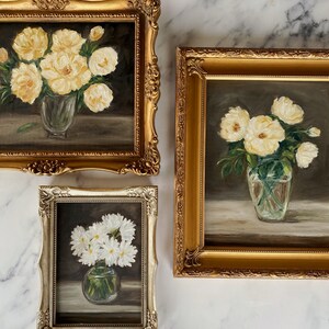 May include: Three framed paintings of white flowers in vases. The paintings are in gold and silver frames. The flowers are in different stages of bloom.