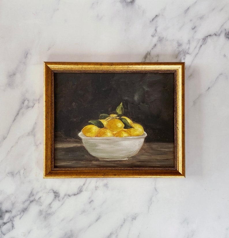 May include: A framed painting of a white bowl filled with yellow lemons and green leaves on a dark background.