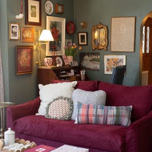 May include: A burgundy velvet sofa with a variety of patterned throw pillows. The sofa is in a living room with a wall decorated with framed artwork and a mirror.