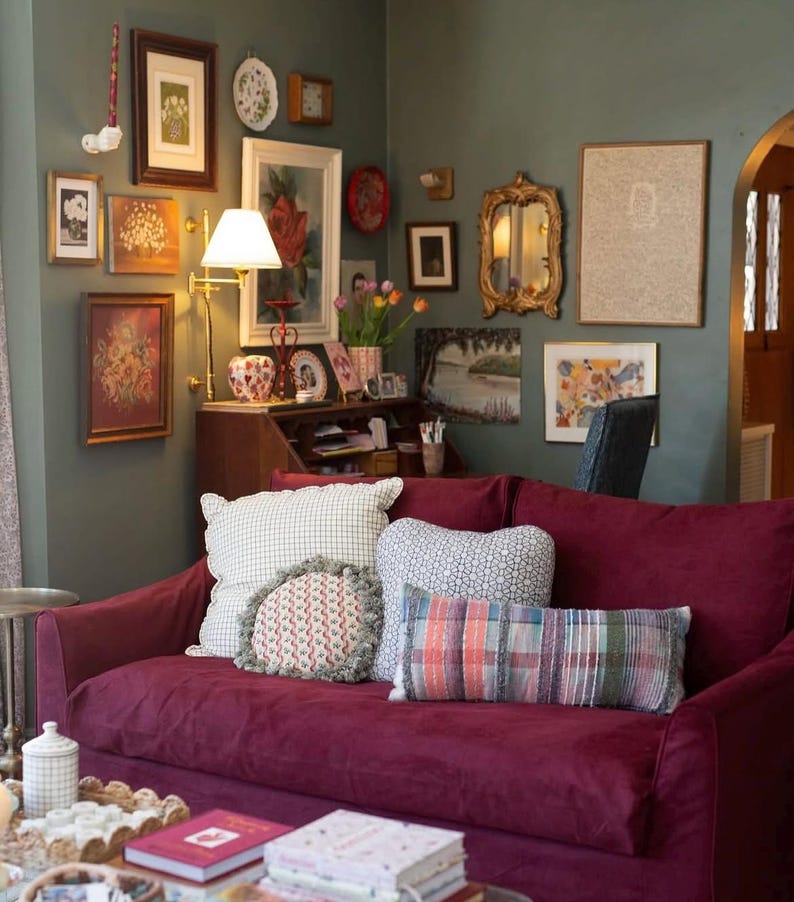 May include: A burgundy velvet sofa with a variety of patterned throw pillows. The sofa is in a living room with a wall decorated with framed artwork and a mirror.