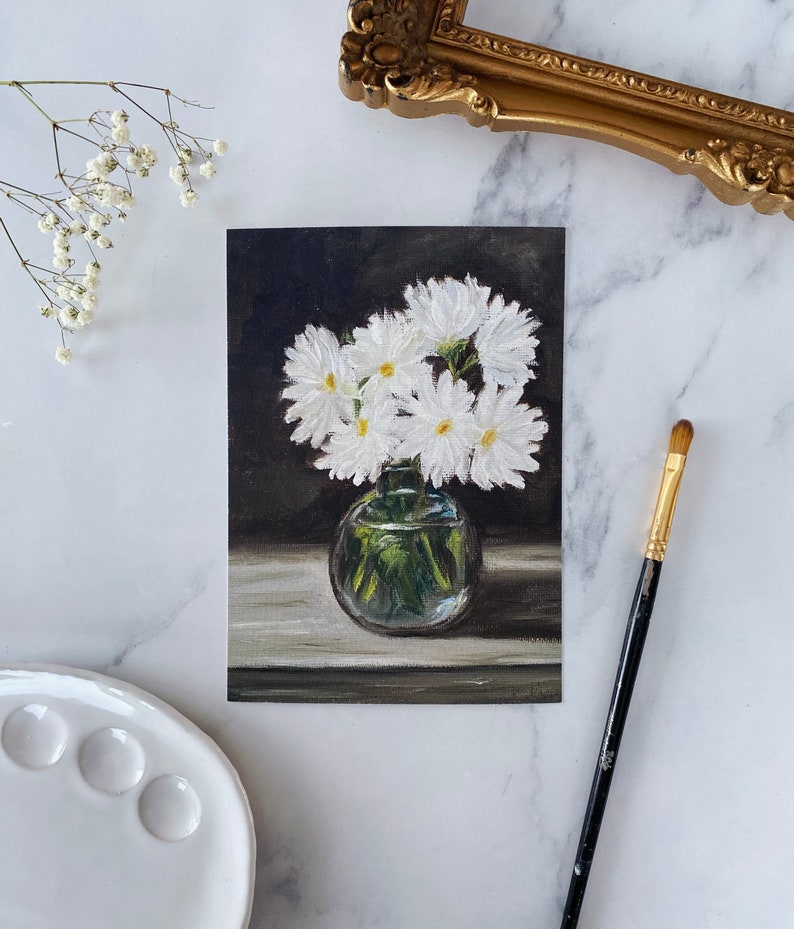 May include: A painting of a bouquet of white daisies in a clear glass vase on a dark background.