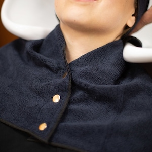 May include: A dark blue towel wrap with gold buttons, designed to protect clothing during hair treatments.