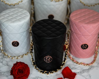 May include: Three quilted cylinder boxes with gold chains and a rose gold logo. The boxes are white, black, and pink.