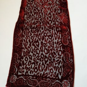 Puede incluir: Una bufanda burdeos con un estampado de leopardo y un borde de cachemira. La bufanda está hecha de una tela suave y transparente, y el estampado de leopardo es de un tono burdeos más oscuro. El borde de cachemira añade un toque decorativo.