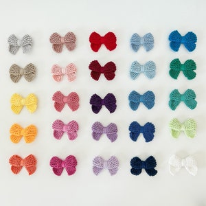 Puede incluir: Una colección de 30 lazos para el pelo de punto en varios colores, incluyendo rojo, azul, verde, morado y blanco. Los lazos están dispuestos en filas sobre un fondo blanco.