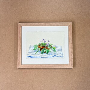 May include: A watercolor painting of a potted plant with purple flowers on a blue and white striped tablecloth. The plant is in a brown pot and the flowers are in bloom.