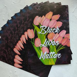 May include: A collection of art prints displaying a watercolour illustration of pink and orange tulips with green stems and leaves. The words "Black Lives Matter" are written in white script.
