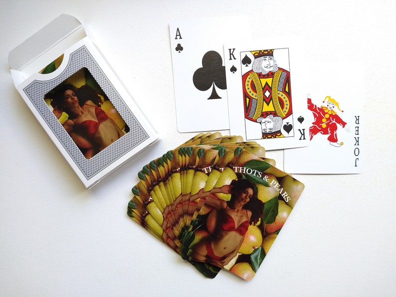 May include: A deck of playing cards with a woman in a red bra and a pear design on the back of the cards. The cards are fanned out and the text on the back of the cards reads "Thots & Pears".