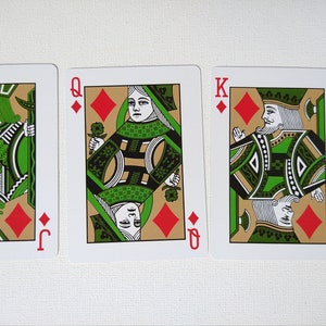 May include: Three playing cards from a deck of cards. The cards are the Jack, Queen, and King of Diamonds. The cards have a green and gold design with a red diamond in the corner.