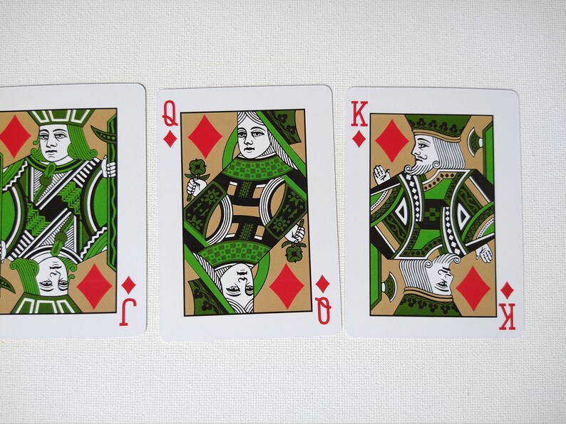 May include: Three playing cards from a deck of cards. The cards are the Jack, Queen, and King of Diamonds. The cards have a green and gold design with a red diamond in the corner.
