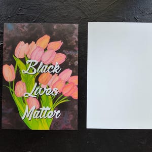 May include: A greeting card featuring a bouquet of pink and orange tulips with green leaves, and the text "Black Lives Matter." The background is dark and textured. A blank white card is next to it.