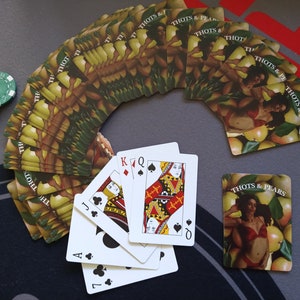 May include: A deck of playing cards with a design of pears and women on the back of the cards. The cards are fanned out in a semi-circle.  The cards are arranged in a semi-circle with the face cards of a standard deck of cards in the center. The face cards are the Jack, Queen, King, and Ace of Spades.