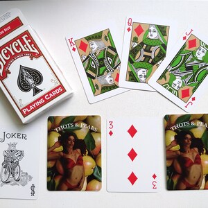 May include: A set of playing cards featuring a standard deck of Bicycle playing cards, a joker card, and four cards from a deck of Thoth & Pears playing cards. The Thoth & Pears cards feature a woman in a red bikini surrounded by pears.