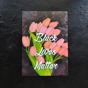 May include: An art print showing a bouquet of pink and orange tulips with green stems and leaves. The words "Black Lives Matter" are written in white script across the image, set against a dark background.