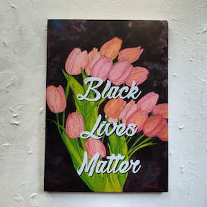 May include: An art print showing a bouquet of pink and orange tulips with green stems and leaves against a dark background. The words "Black Lives Matter" are written in white script across the image.