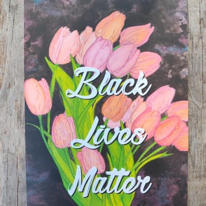 May include: An art print showing a bouquet of pink and peach tulips with green leaves against a dark backdrop. The words "Black Lives Matter" are written in white script across the image.
