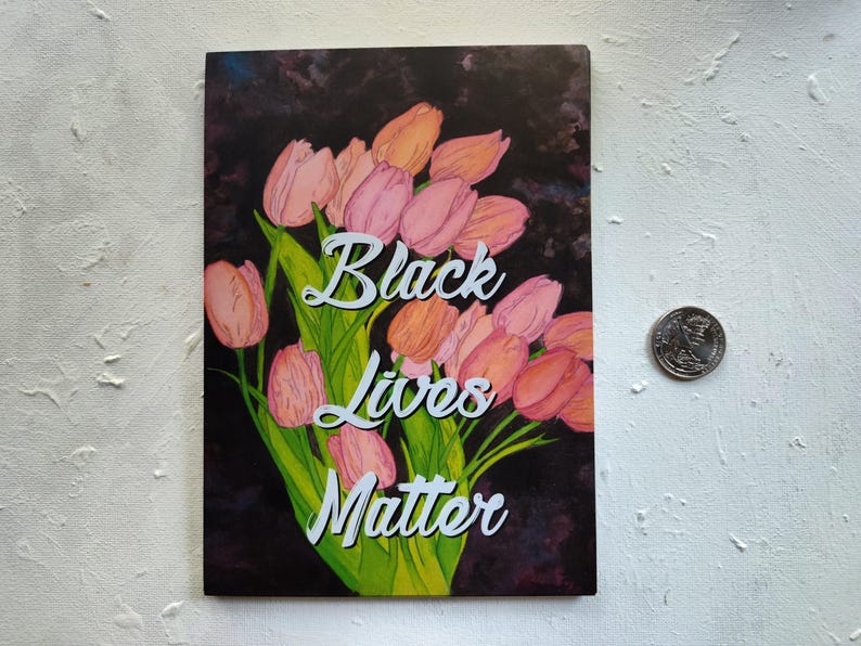 May include: An art print showing a bouquet of pink and orange tulips on a dark backdrop. The words "Black Lives Matter" are in white script. A coin is next to the print. The print is rectangular.