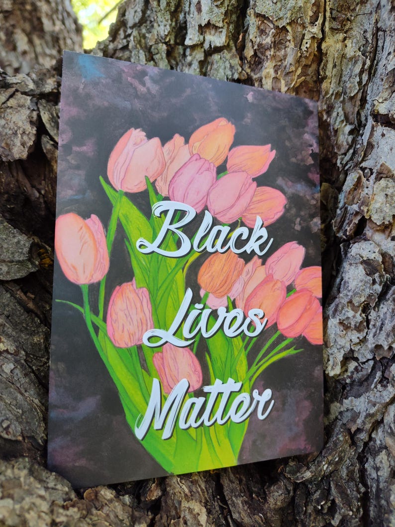 May include: A card displaying a floral arrangement of pink and orange tulips with green foliage, set against a dark backdrop. The words "Black Lives Matter" are written in white script. The card is shown against a textured tree trunk.