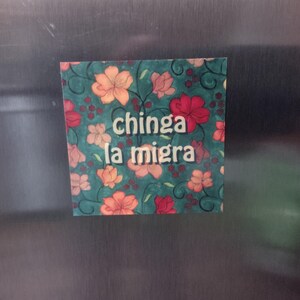 Puede incluir: Un im&aacute;n con un dise&ntilde;o floral y el texto "chinga la migra" en letras blancas.