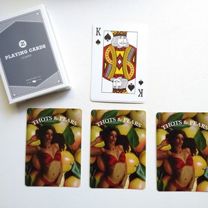 May include: Three playing cards with a woman in a red bikini lying on a bed of pears. The cards are labeled "Thots & Pears".
