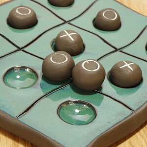 May include: A green and brown ceramic tic-tac-toe game with brown ceramic pieces. The pieces have either an 'X' or an 'O' painted on them.