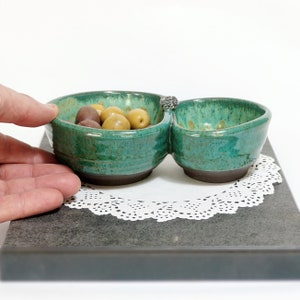 May include: A green ceramic serving dish with two divided sections. The dish is filled with green and brown olives.