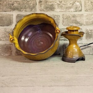 May include: A yellow and brown ceramic bowl with a wavy rim and a brown ceramic water fountain with a yellow glaze.