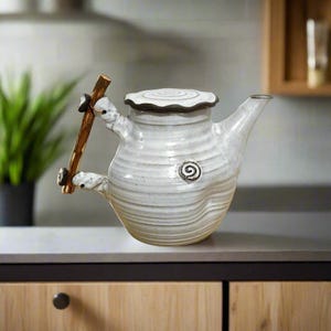 May include: White ceramic teapot with a wooden handle and lid. The teapot has a textured surface and a spiral design on the side.