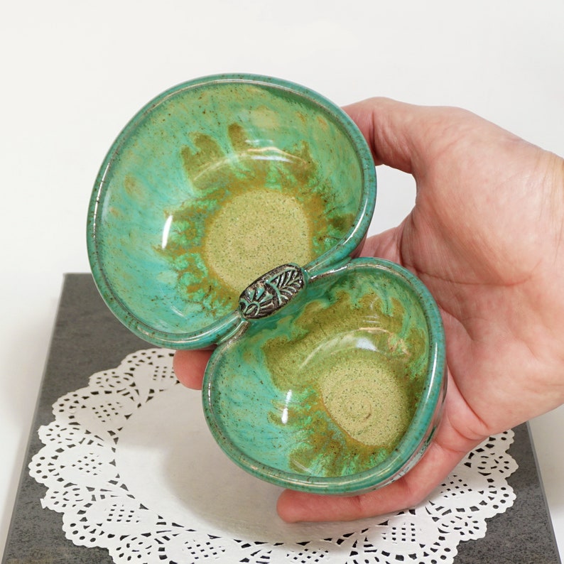 May include: A green and brown ceramic double dish with a decorative handle. The dish is glazed with a mottled green and brown finish.