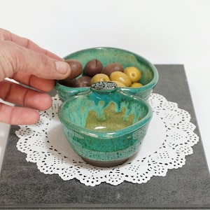 May include: A teal green ceramic serving dish with two bowls. The dish has a leaf design on the top. The bowls are filled with green and brown olives.
