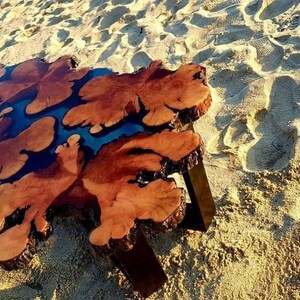 May include: A wooden coffee table with a unique, natural, live edge design. The table top features a dark brown wood with blue resin filling in the natural cracks and knots. The table has a simple, modern design with black metal legs.
