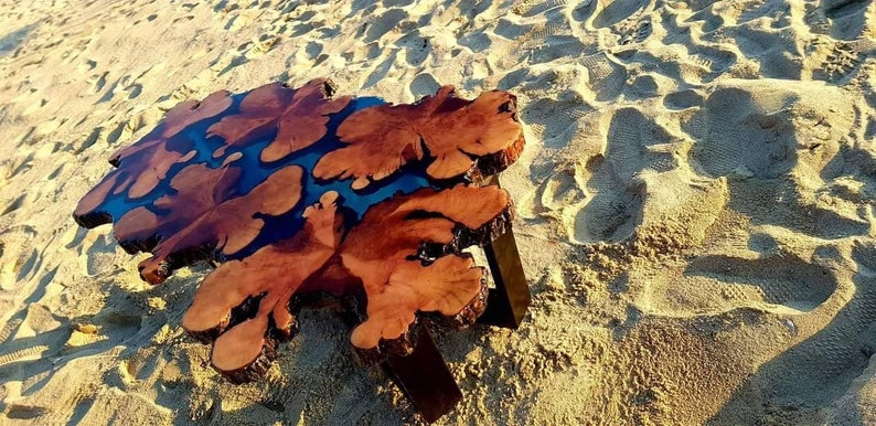 May include: A wooden coffee table with a unique, natural, live edge design. The table top features a dark brown wood with blue resin filling in the natural cracks and knots. The table has a simple, modern design with black metal legs.