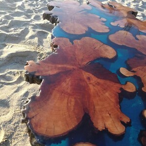 May include: A large wooden slab with a natural edge, filled with blue epoxy resin. The resin creates a unique pattern of swirls and shapes, resembling a river or lake.