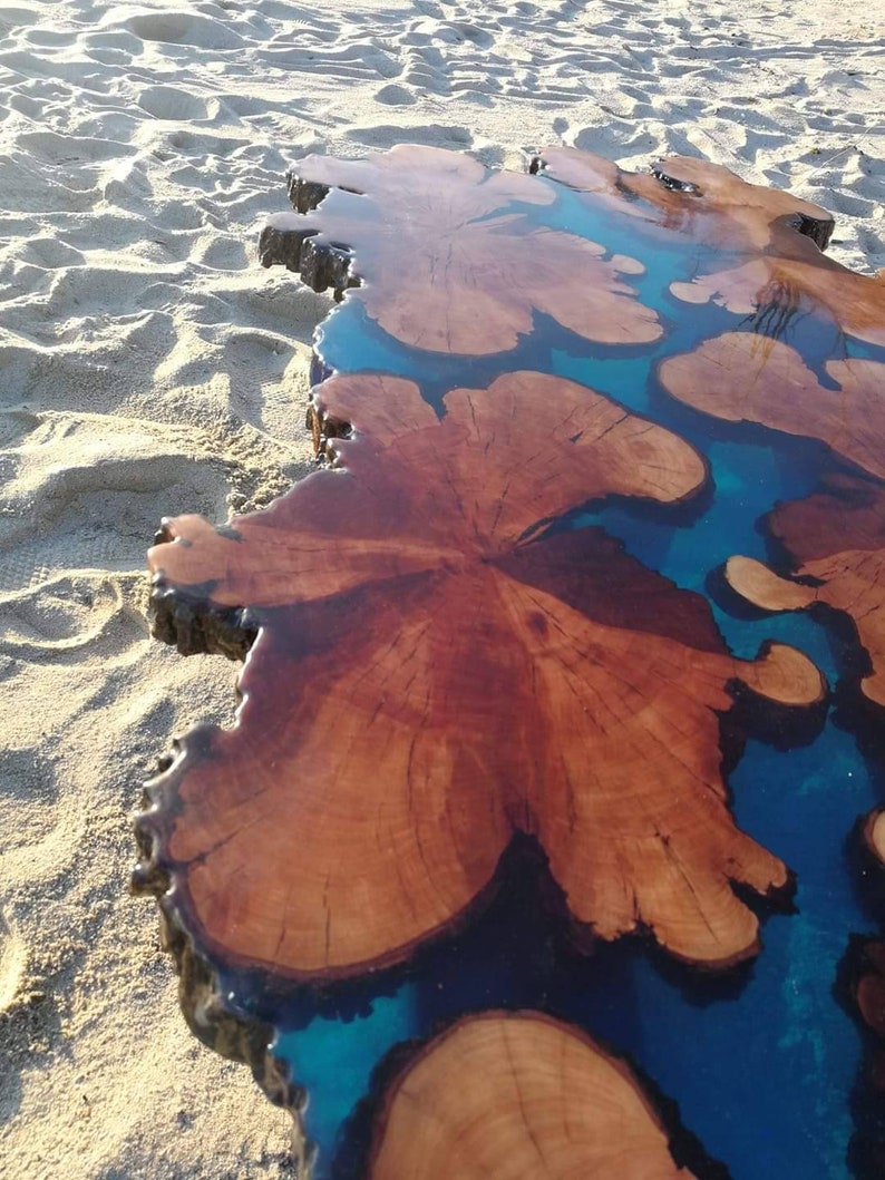 May include: A large wooden slab with a natural edge, filled with blue epoxy resin. The resin creates a unique pattern of swirls and shapes, resembling a river or lake.