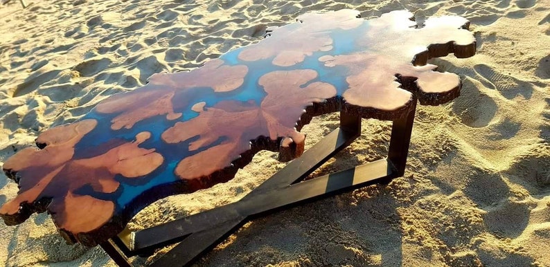 May include: A unique coffee table with a live edge wooden top and a blue epoxy resin inlay. The table has a black metal X-shaped base.