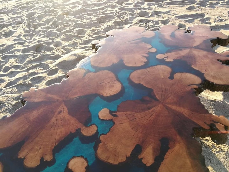 May include: A large wooden slab with a natural wood grain pattern, filled with blue epoxy resin. The resin creates a unique, flowing design.