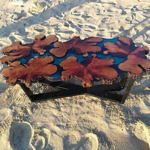 May include: A unique coffee table with a live edge wooden top and a blue resin inlay. The table has a black metal base with a cross-shaped design.