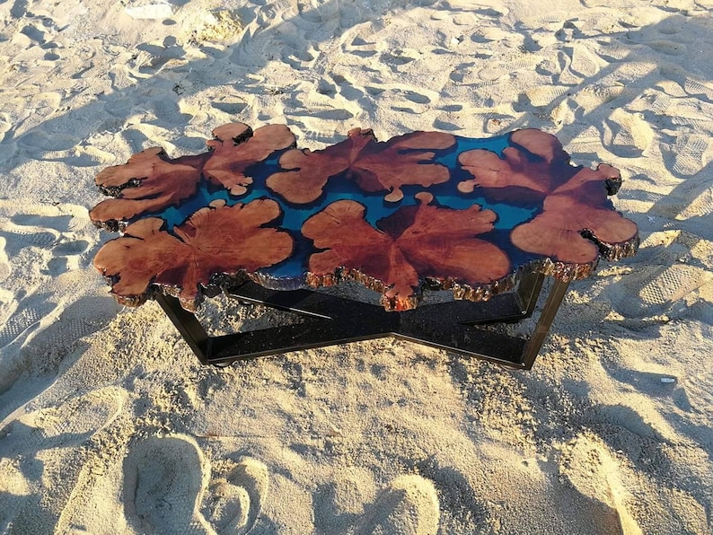 May include: A unique coffee table with a live edge wooden top and a blue resin inlay. The table has a black metal base with a cross-shaped design.