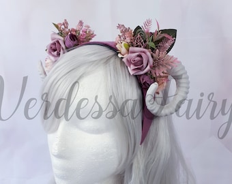 May include: A purple headband with white horns and pink flowers. The headband is decorated with pink roses, greenery, and small pink flowers. The text "Verdessea Fairy" is visible in the background.