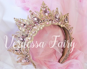 May include: A gold crown headband with pink and clear rhinestones. The headband is on a pink and white tulle fabric.