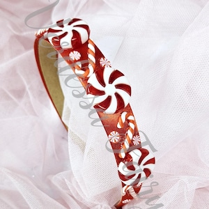 May include: A festive headband with a red and white candy cane and peppermint design. The headband features large, white and red peppermint candies and smaller candy cane accents. The base is a reddish-orange colour.