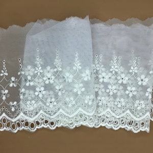 May include: White embroidered lace trim with a scalloped edge and a delicate floral pattern. The lace is made of a sheer fabric and is perfect for adding a touch of elegance to any project.