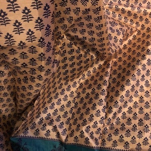 May include: A close-up of a fabric with a repeating pattern of black floral designs on a light brown background. The fabric has a green border with a black floral design.